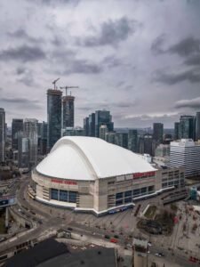 Large stadium with a dome, high-rise buildings, cranes, and overcast sky. "Rogers Centre" visible.