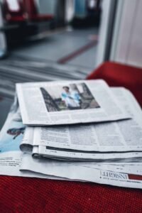 Stack of newspapers on red fabric in a public seating area, top one showing a blurred image.