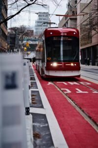 Red streetcar on a city track, surrounded by buildings, on a red-marked streetcar-only path.