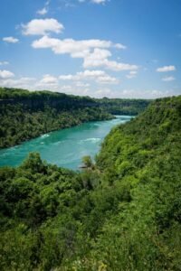 River flowing between green forests under a blue sky with clouds.