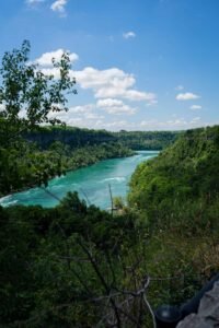 Winding river amidst lush green trees under a blue sky with scattered clouds.