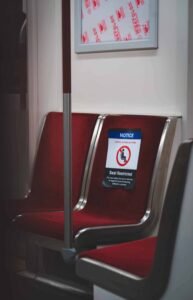 Red transit seats, one with COVID-19 restriction sign, pole and signage frame visible.