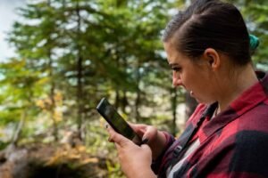 Person in red plaid shirt using smartphone outdoors, with trees in the background.