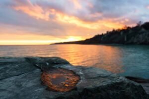 Coastal sunset with rocky foreground, puddle, calm sea, and vibrant sky colors.