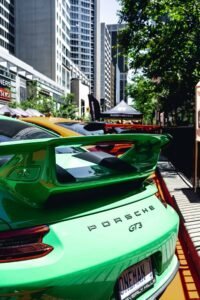 Green Porsche GT3 parked in urban area, high-rise buildings and trees in background.
