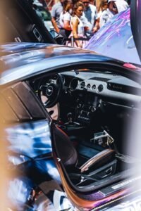 Interior of a sports car with open door, visible dashboard; people in the background.