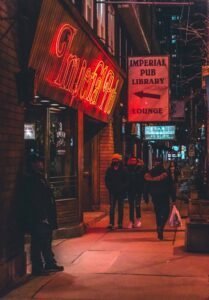 Street scene at night with people near the neon-lit Imperial Pub, Library, and Lounge signs.