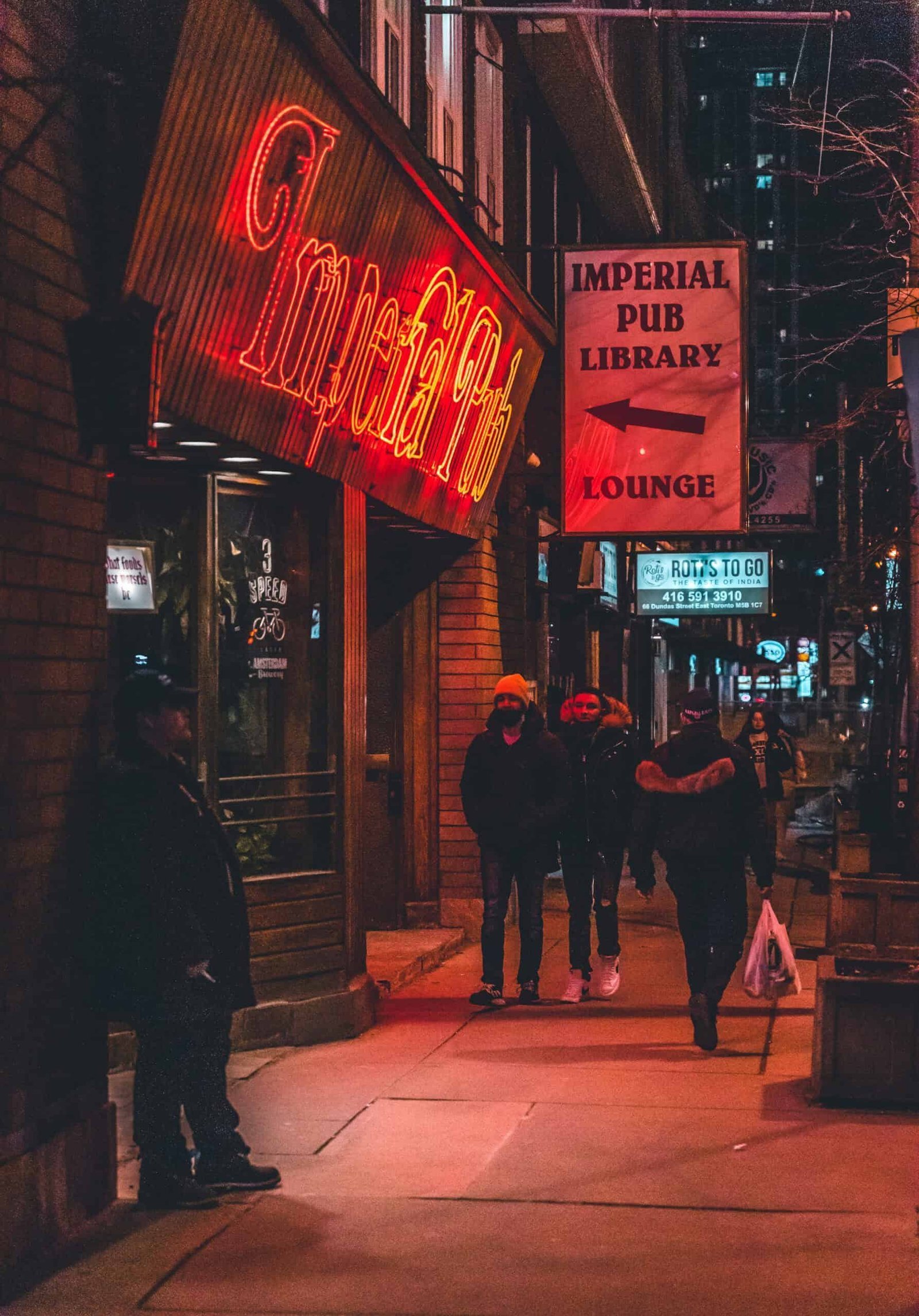 Street scene at night with people near the neon-lit Imperial Pub, Library, and Lounge signs.
