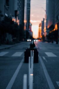 City street at sunset with blurred road dividers, warm light on tall buildings in background.