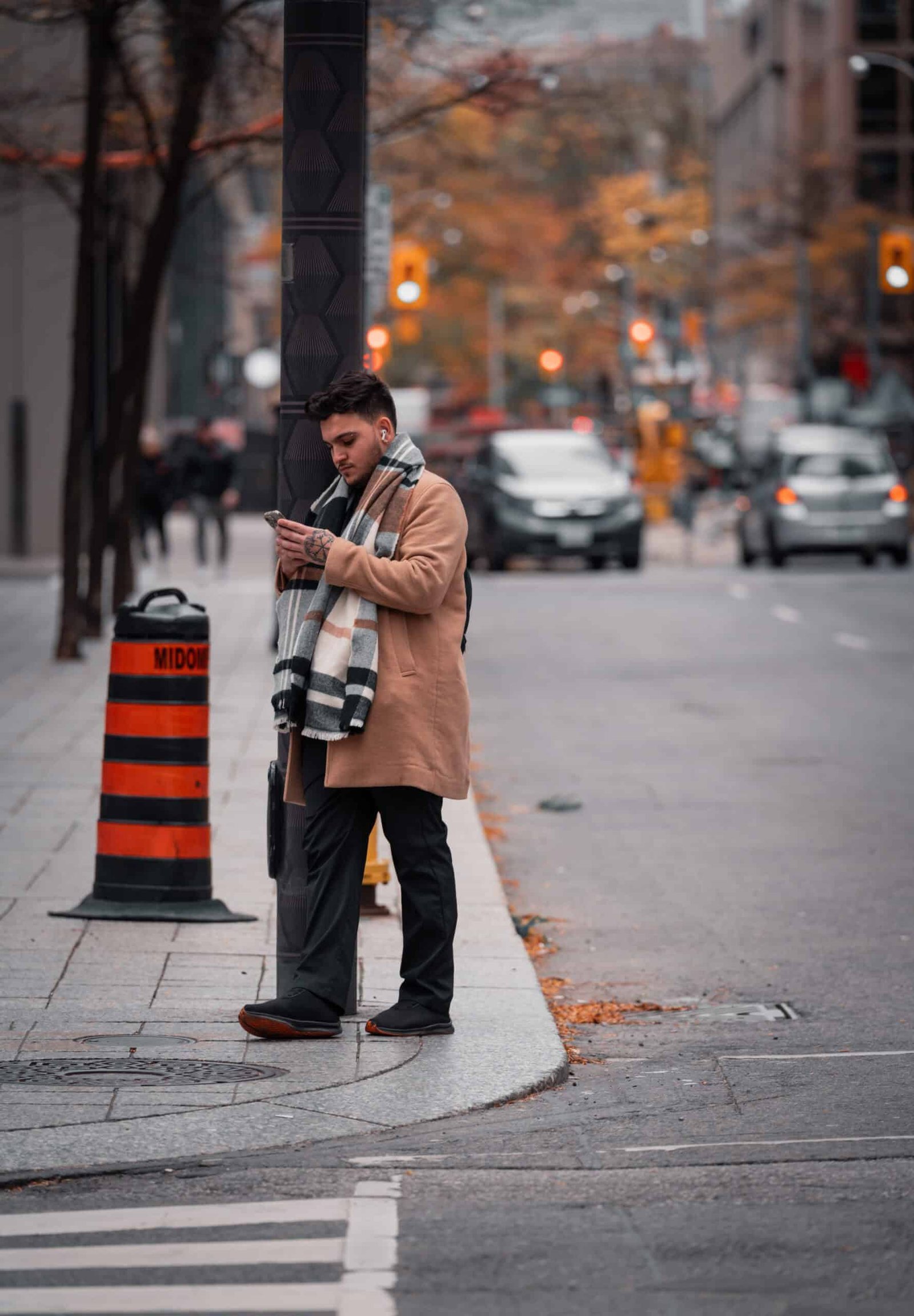 An image of a man looking at his phone while leaning on a light post at a Toronto Intersection