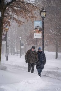 Two people walk through snow at University of Toronto with banner and streetlights visible.